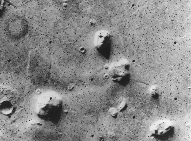 A grainy orbital photograph of a mesa in Cydonia whose shadows suggest eyes, a nose and a mouth.
