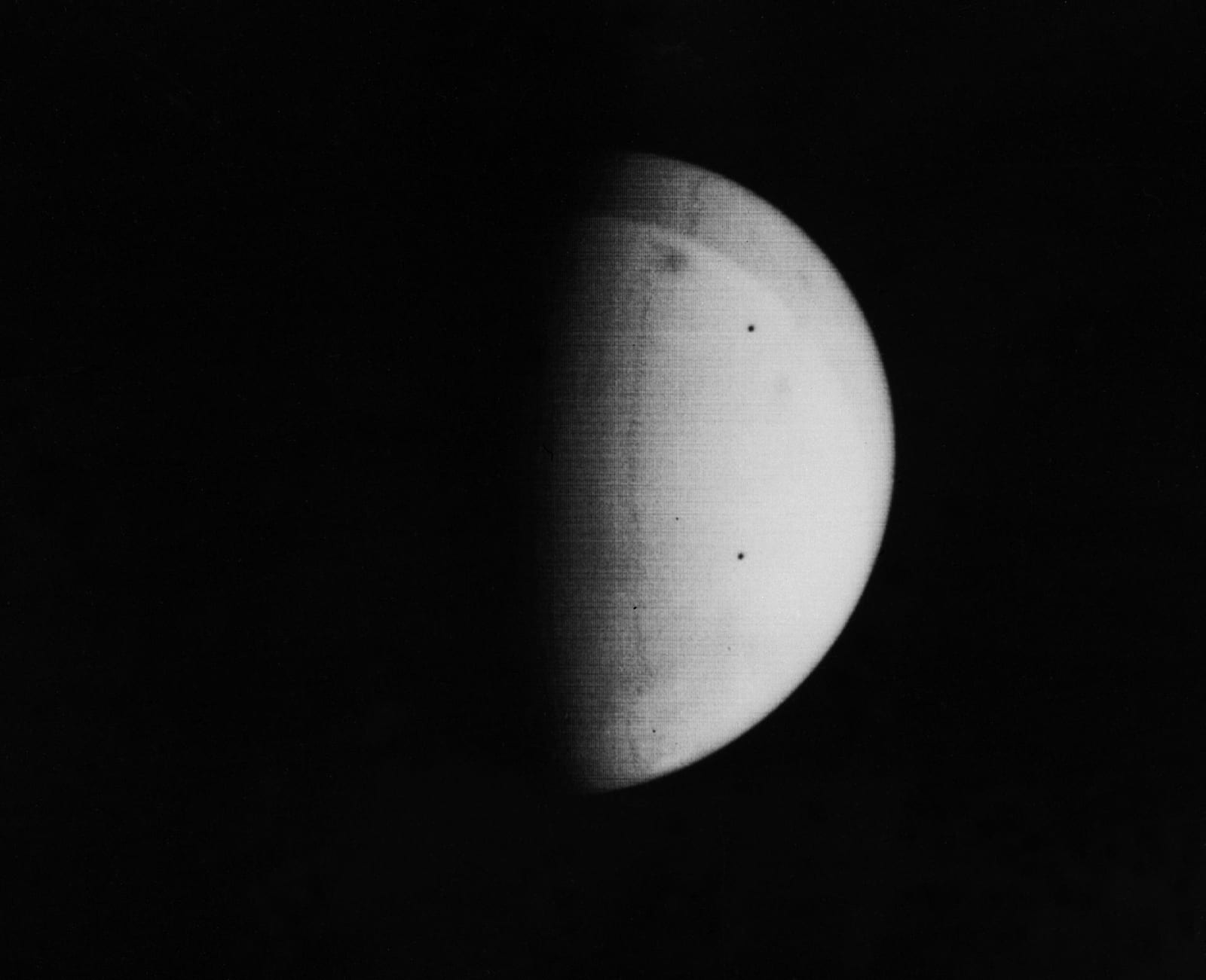 A crescent of Mars almost featureless with dust, with a few dark spots breaking through the haze.