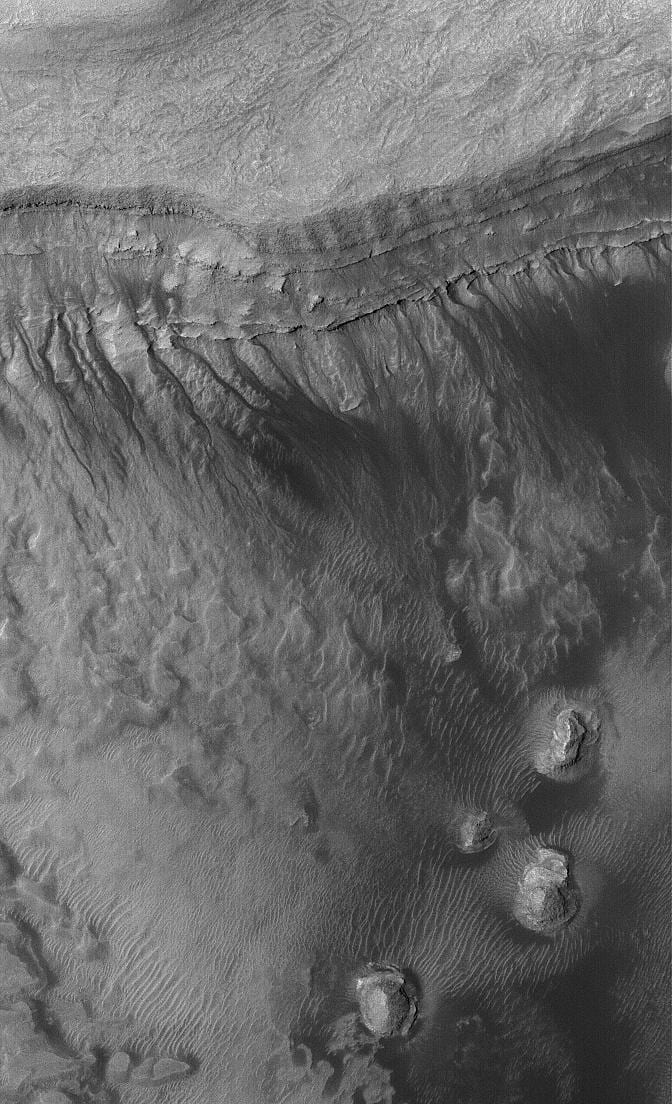 A high-resolution orbital view of a crater wall cut by narrow branching gullies that end in debris fans.