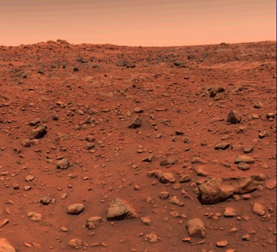 A rock-strewn orange plain under a pale sky, photographed from just above ground level.